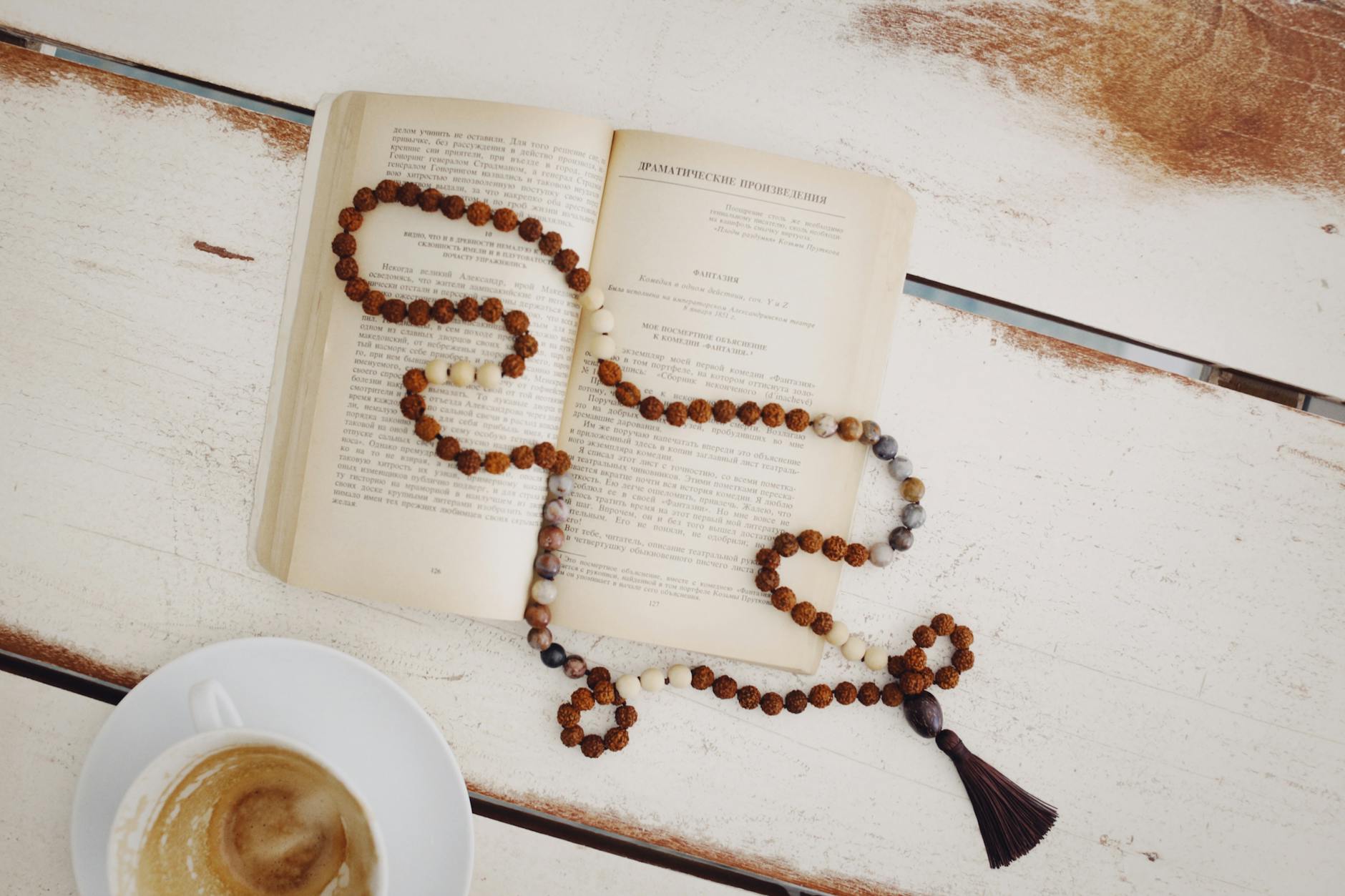 an open book with mala necklace on top near a cup of coffee